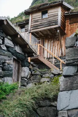 a wooden cabin with a staircase on the side of a stone building at Ein heilt spesiell låve i Røldal in Røldal