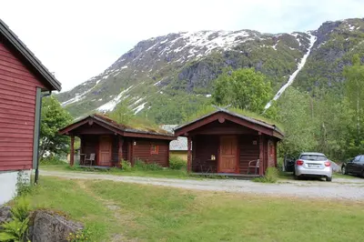 two wooden buildings with grass on their roofs in front of a mountain at Skysstasjonen Cottages in Røldal