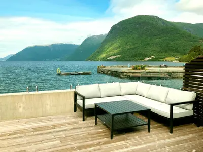 a couch and a table on a deck next to the water at Havila Hotel Raftevold in Hornindal