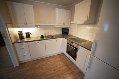 a kitchen with white cabinets and a sink and a refrigerator at Førde Gjestehus og Camping in Førde