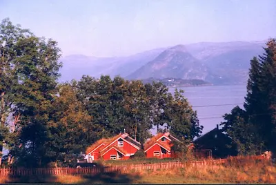 two red houses on a hill with mountains in the background at Hardanger Feriesenter Nesvika in Norheimsund