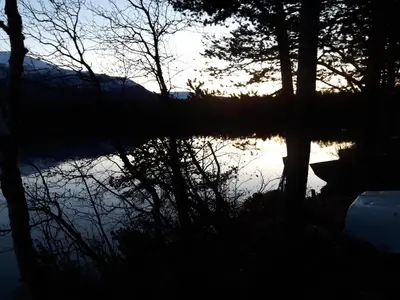 a reflection of the sun in a lake with trees at Lesjaskogsvatnet Camping in Lesjaskog