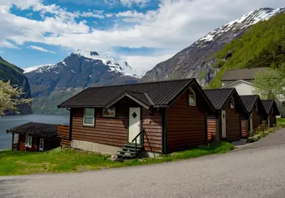 a row of wooden cabins with mountains in the background at Grande Hytteutleige og Camping in Geiranger