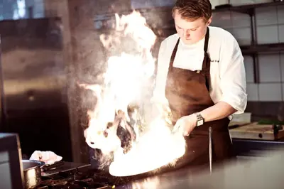 a man in a kitchen cooking food on a grill at Fossheim Hotel Lom in Lom