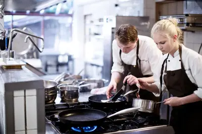 two women in a kitchen preparing food on a stove at Fossheim Hotel Lom in Lom