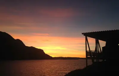 a sunset over a body of water with a house at Værlandet Havhotell in Hamna