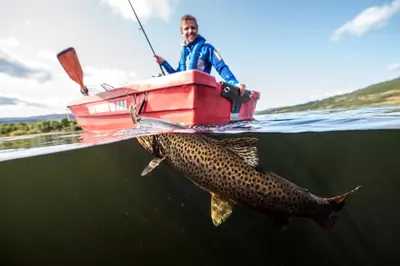 a man in a boat with a large fish in the water at Gomobu Fjellstue in Ron