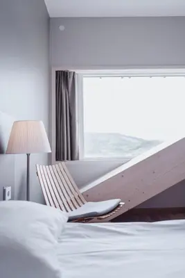 a bedroom with a bed and a window with a chair at Wood Hotel by Frich's in Brumunddalen