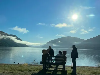 a group of people sitting on a bench by a lake at Sandviken Camping in Austbygdi