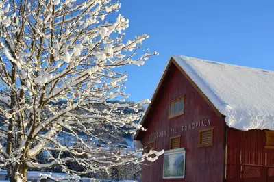 a snow covered tree next to a red barn at Sandviken Camping in Austbygdi