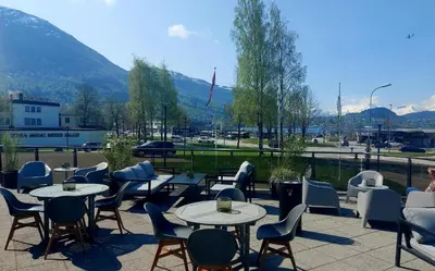 a patio with tables and chairs with mountains in the background at Havila Hotel Ivar Aasen in Ørsta