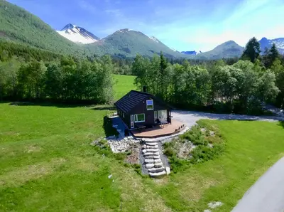 a small cabin in a field with mountains in the background at Heinåli Hytta in Isfjorden