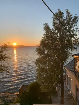 a sunset over the water with a house and a tree at Seaside Rentals in Trondheim