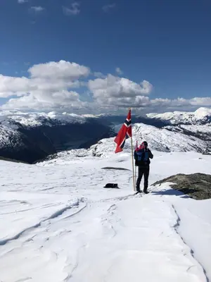 a man standing on top of a mountain with a flag at Akrafjorden Nature B&B AS in Fjæra