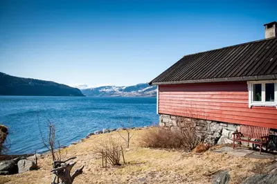 a red building with a bench next to a body of water at Bodvarstova in Stryn