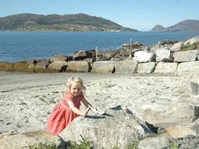 a little girl in a red dress sitting on a beach at 6 person holiday home in Åram-By Traum in Sandvik