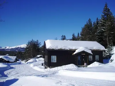 a small house covered in snow with trees and mountains at Hogstul Hytter - Gamlestua in Tuddal