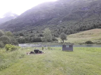 a building in a field next to a river at Naustvoll in Olden