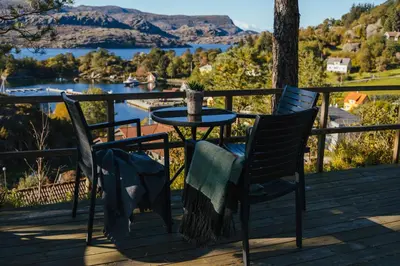 a table and chairs on a deck with a view of a lake at Solund Leileghetshotell in Hardbakke