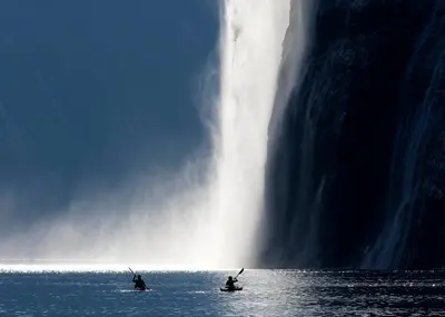 two people in the water in front of a waterfall at Geirangerfjorden Feriesenter in Geiranger