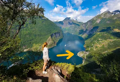a woman standing on top of a cliff looking at a lake at Geirangerfjorden Feriesenter in Geiranger