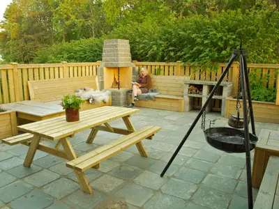 a man sitting next to a picnic table and a fire pit at Kårstua - Austrått Agroturisme in Austrått