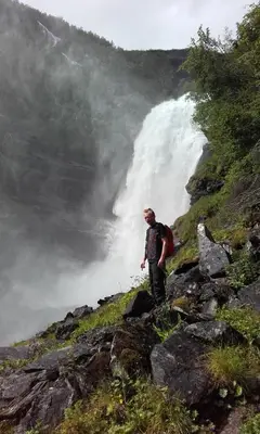 a man standing on top of a mountain near a waterfall at Vassbakken Kro og Camping in Skjolden