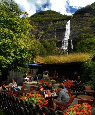 a group of people sitting at tables in front of a waterfall at Vassbakken Kro og Camping in Skjolden