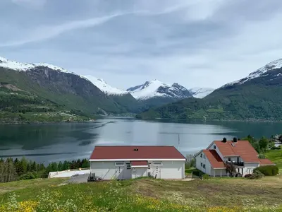 a house on a hill next to a lake with mountains at Olden Fjord Apartments in Olden