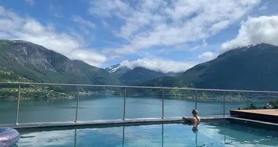 a person in a swimming pool with a view of mountains at Olden Fjord Apartments in Olden