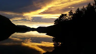 a sunset over a body of water with a cloudy sky at Naustloftet in Hornindal