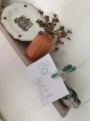 a table with a plate and a vase and a sign at Olsens Pensjonat in Veiholmen