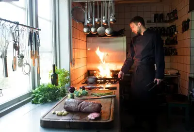 a man in a kitchen preparing food in a stove at Nutheim Gjestgiveri in Flatdal