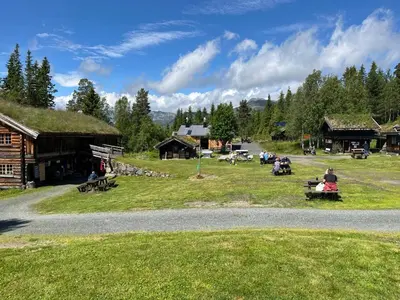 a group of people sitting on benches in a field next to buildings at Raulandsakademiet in Rauland