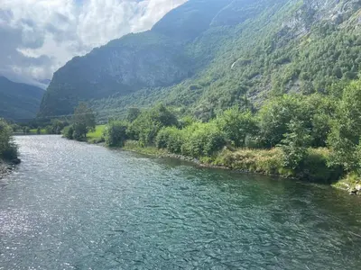 a river in front of a valley with mountains at Brekke Gard Hostel in Flåm