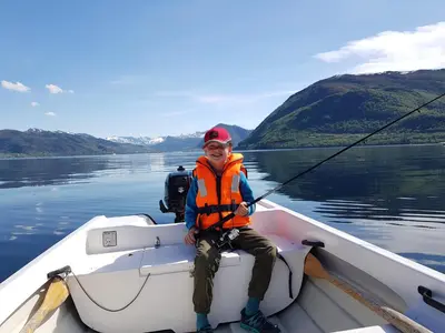 a young boy sitting in a boat holding a fishing pole at Irenegarden - Panorama apartment in Lauvstad