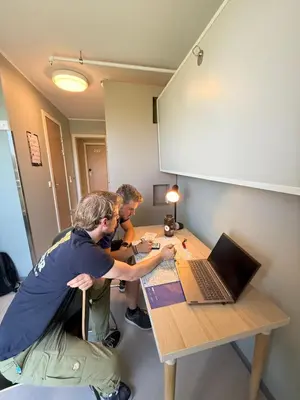 three men sitting at a table with a laptop at Bergen Hostel Montana in Bergen