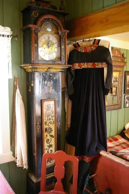 a large grandfather clock next to a bed with a dress at Hagaled Gjestegård in Nesbyen