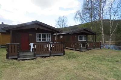 a small cabin with a deck and a lake at Camp Uvdal in Uvdal