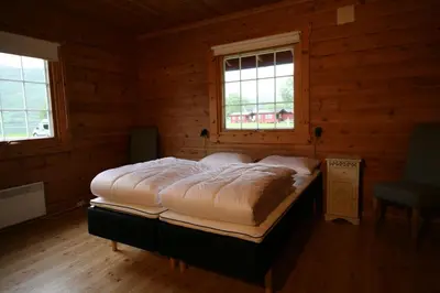 a bed in a wooden room with two windows at Bøflaten Camping AS in Vang I Valdres