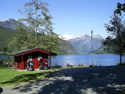 a red shed with a motorcycle parked next to a lake at Mindresunde Camping in Mindresunde