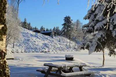 a wooden picnic table covered in snow next to a river at Trysil Motell & Vandrerhjem in Trysil