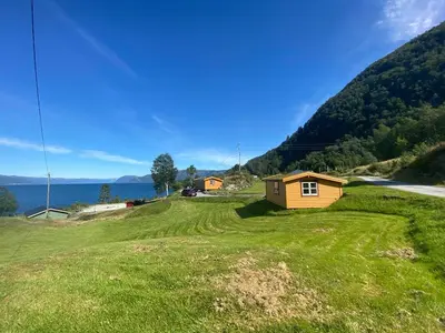 a small house on a grassy hill next to the ocean at Botnen Camping in Botnen