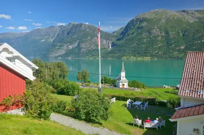 a view of a lake with a red house and a church at Nes Gard in Høyheimsvik
