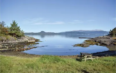 a wooden bench sitting on the side of a lake at Lovely Home In Skånevik in Skånevik