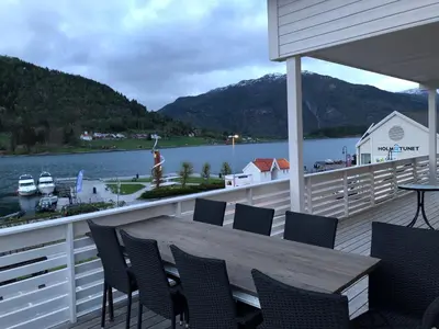 a deck with a wooden table and chairs on the water at Balestrand Fjordapartments in Balestrand