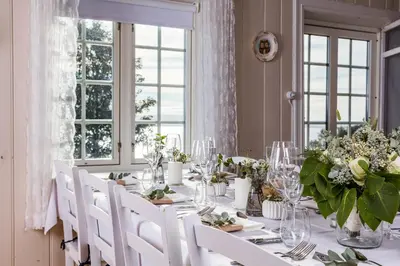 a dining room with a table with white chairs and flowers at Husfrua Gårdshotell in Straumen