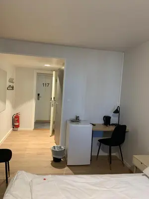 a room with a bed and a desk and a refrigerator at Husnes Sentrum Hotell in Husnes