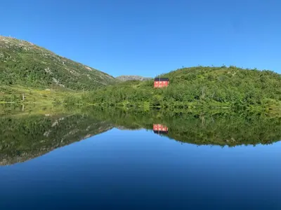 a red house on a hill next to a lake at Høyanger 3 roms leilighet in Høyanger