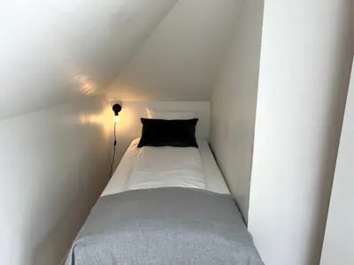 a small bed in a white room with a black pillow at Fabryka in Bergen